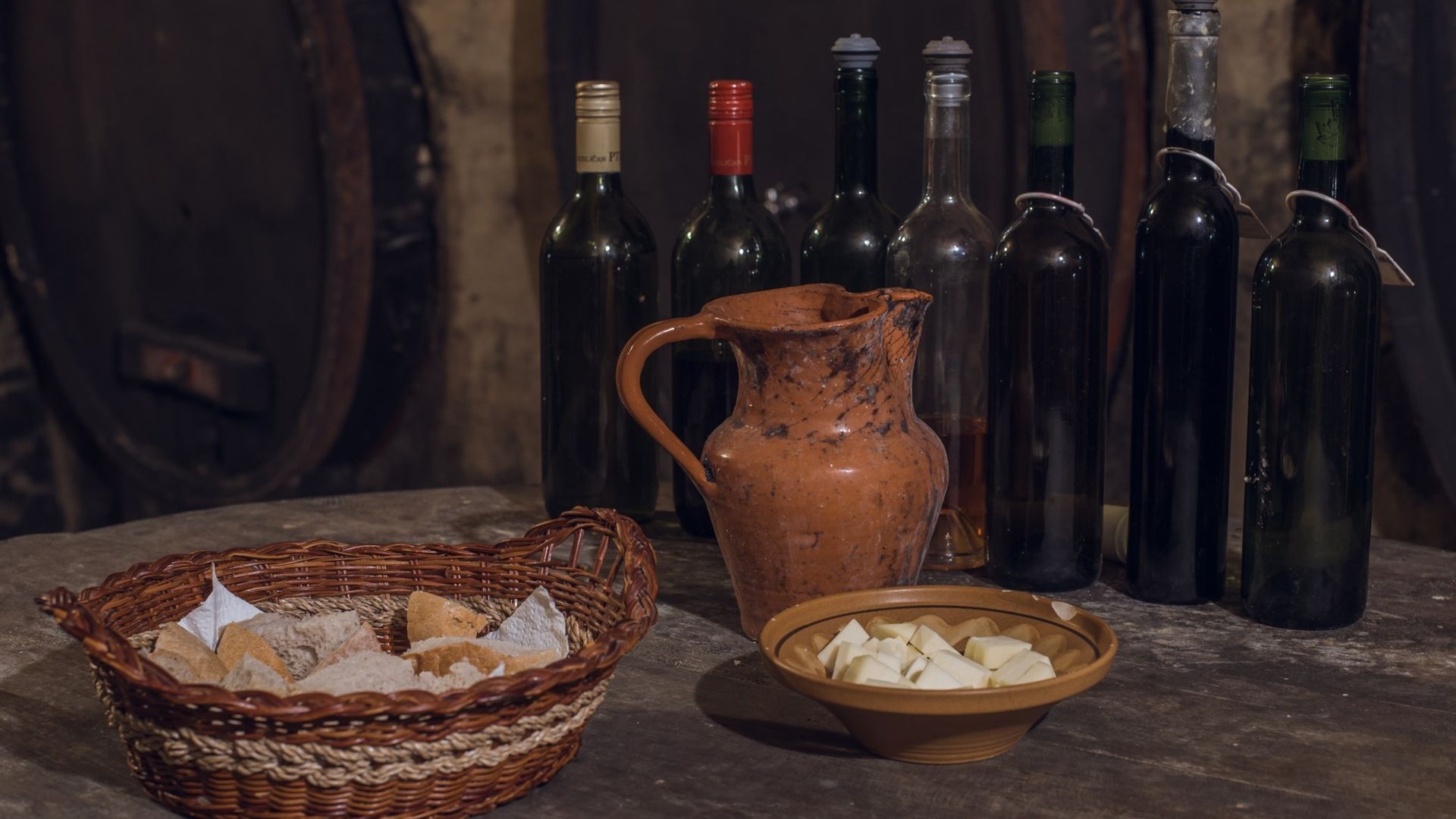 Fotografija mize s kruhom, sirom, vinom in loncem.